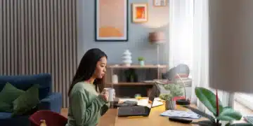 Mulher trabalhando em casa com um computador portátil, mantendo uma xícara de café, em ambiente tranquilo e moderno