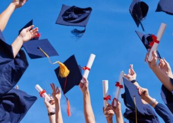 Formatura universitária com pessoas jogando chapéus e segurando diplomas ao céu, simbolizando a celebração de conquista acadêmica.