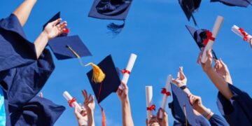 Formatura universitária com pessoas jogando chapéus e segurando diplomas ao céu, simbolizando a celebração de conquista acadêmica.