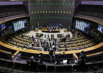 Visão ampla do plenário da Câmara dos Deputados com deputados em sessão e painéis digitais nas paredes