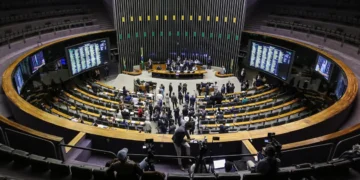 Visão ampla do plenário da Câmara dos Deputados com deputados em sessão e painéis digitais nas paredes