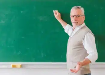 Professor sênior explicando na lousa verde, representando a importância do docente no Brasil.