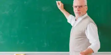 Professor sênior explicando na lousa verde, representando a importância do docente no Brasil.