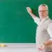 Professor sênior explicando na lousa verde, representando a importância do docente no Brasil.