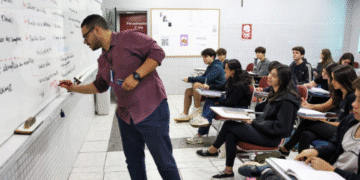 Professor escreve no quadro enquanto alunos assistem à aula e fazem anotações em sala de aula.