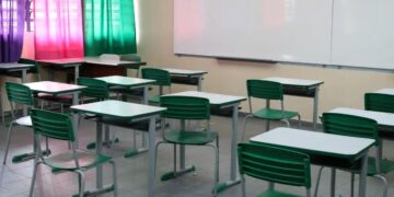 Sala de aula vazia com carteiras e cadeiras verdes em frente a uma lousa branca, simbolizando o local de realização da Prova Nacional Docente (PND).