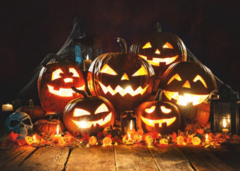 Abóboras iluminadas com rostos esculpidos e decoração típica de Halloween sobre uma mesa de madeira.