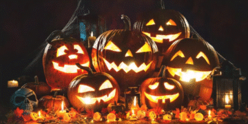 Abóboras iluminadas com rostos esculpidos e decoração típica de Halloween sobre uma mesa de madeira.