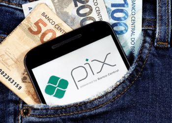 Notas de 50, 100 e 200 reais e smartphone com logo do Pix no bolso de uma calça jeans.