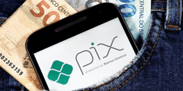 Notas de 50, 100 e 200 reais e smartphone com logo do Pix no bolso de uma calça jeans.