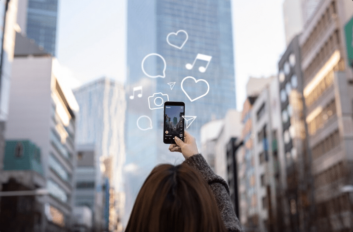 Usuário de celular em ambiente urbano checando as redes sociais, com ícones de curtidas e mensagens, simbolizando a intensa conexão e a influência das plataformas na criação de relações parassociais.