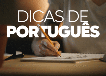 Mão de pessoa branca escrevendo "Dicas de Português" com lápis em caderno com fundo escuro.