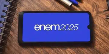 Celular com logo do ENEM 2025 na tela azul sobre mesa de madeira com caderno e canetas ao lado