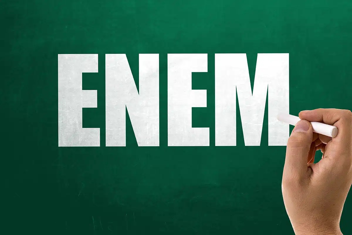 ENEM 2025: Divulgação Oficial de Gabaritos e Cadernos de Questões Palavra ENEM escrita em letras maiúsculas e brancas com giz em um quadro-negro verde, com uma mão segurando um pedaço de giz na direita.