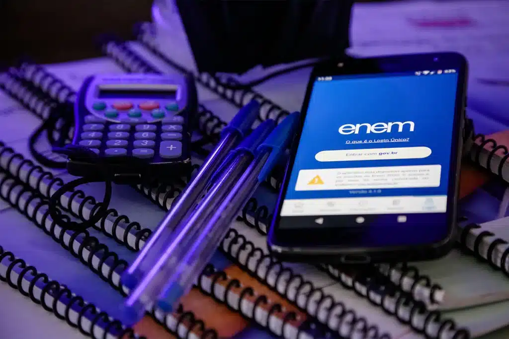Preparação para o Enem 2025: Ferramentas e Prazos de Reaplicação Celular exibe tela de login do Enem (Entrar com gov.br) ao lado de calculadora, canetas azuis e cadernos espirais, simbolizando a preparação e a gestão de prazos para a reaplicação da prova.