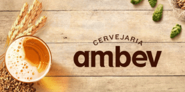 Logo da Cervejaria Ambev ao lado de um copo de cerveja, grãos de cevada e lúpulo sobre superfície de madeira