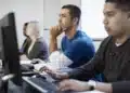 Grupo de estudantes em um curso técnico, concentrados e utilizando computadores.