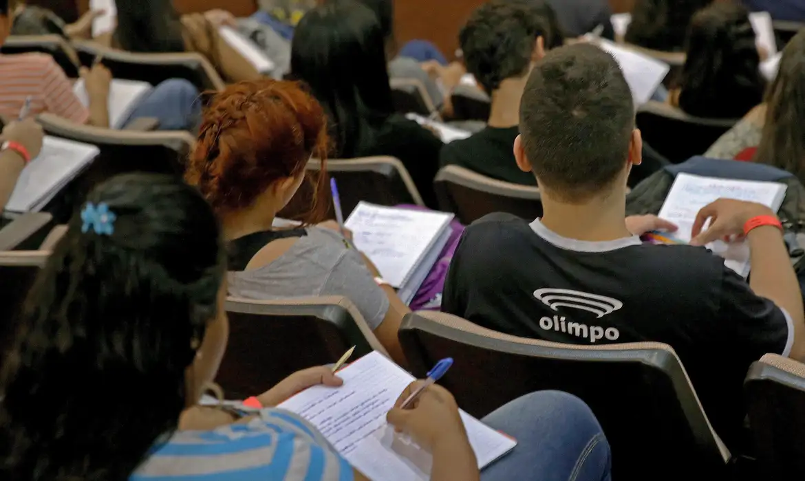 Estudantes em sala de aula anotando conteúdo Alunos sentados em sala de aula escrevendo em cadernos durante aula