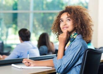 Jovem estudante universitária pensativa e inspirada em sala de aula, refletindo sobre carreira e o futuro do mercado de trabalho com esses cursos em alta.