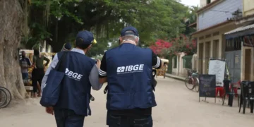 Dois agentes do IBGE caminhando por rua de bairro durante coleta de dados para pesquisa