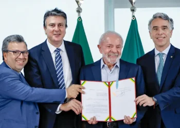 Lula e três políticos segurando documento assinado em cerimônia oficial com bandeiras ao fundo