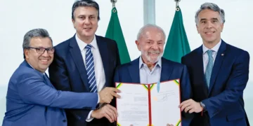 Lula e três políticos segurando documento assinado em cerimônia oficial com bandeiras ao fundo