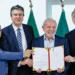 Lula e três políticos segurando documento assinado em cerimônia oficial com bandeiras ao fundo
