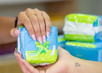 Mãos segurando um pacote de absorventes femininos azul com verde, embalagem com 8 unidades
