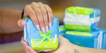 Mãos segurando um pacote de absorventes femininos azul com verde, embalagem com 8 unidades