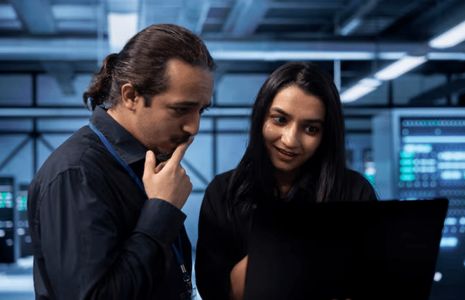 Dois profissionais concentrados analisando informações em laptop dentro do ambiente corporativo moderno