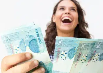 Mulher alegre segurando várias notas de cem reais em fundo branco