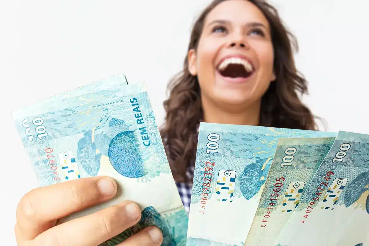 Mulher sorrindo segurando dinheiro em notas de cem reais Mulher alegre segurando várias notas de cem reais em fundo branco