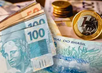 Cédulas de real brasileiro nas denominações de 50 e 100 reais com moedas de 1 real ao fundo