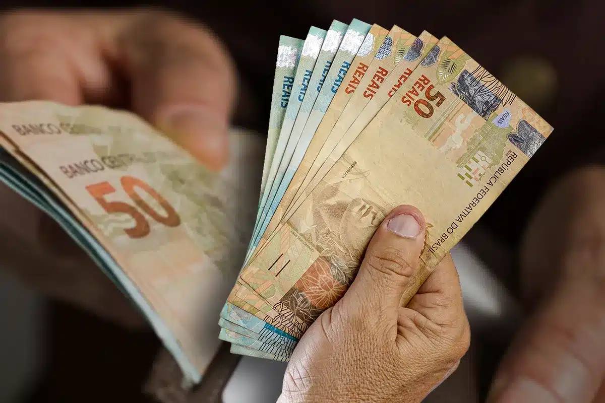 Mão segurando cédulas de dinheiro em reais brasileiros Close de mãos segurando várias cédulas de 50 e 20 reais em posição de contagem