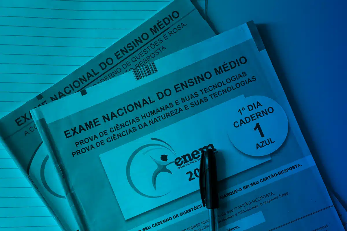 Reaplicação Enem. Cadernos de Questões do Enem, 1º Dia, Caderno 1, cor Azul, com uma caneta preta em cima, representando o início da aplicação das provas.