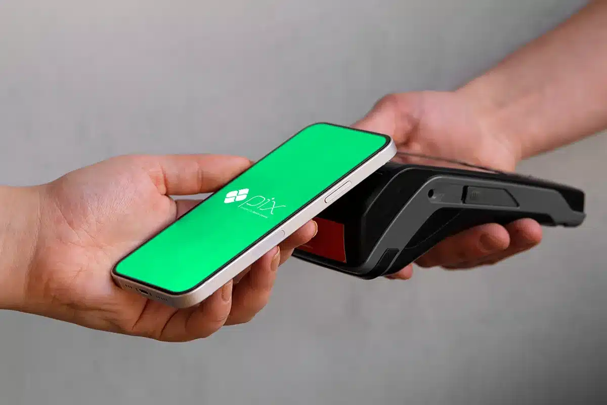 Pagamento de contas via Pix. Imagem de uma pessoa aproximando um smartphone com tela verde e logotipo do Pix de uma maquininha de cartão preta para realizar um pagamento.