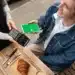 Pessoa pagando com celular via Pix em máquina de cartão em cafeteria com croissant e café na mesa