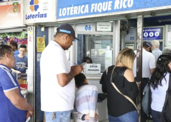 Pessoas esperando em fila na lotérica Fique Rico, com caixa fechado e ambiente movimentado.
