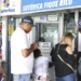 Pessoas esperando em fila na lotérica Fique Rico, com caixa fechado e ambiente movimentado.