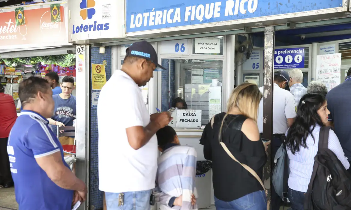 Fila na Lotérica Fique Rico em Atendimento Pessoas esperando em fila na lotérica Fique Rico, com caixa fechado e ambiente movimentado.