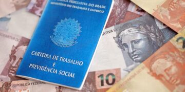 Carteira de trabalho brasileira e notas de dinheiro, representando o impacto do novo salário mínimo e seguro-desemprego em 2026.