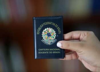 Carteira Nacional Docente do Brasil sendo exibida em primeiro plano por uma pessoa