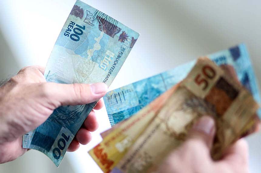 Pessoa segurando cédulas de R$ 100 e R$ 50, representando a circulação de dinheiro no Brasil e o impacto do aumento do salário mínimo em 2026.