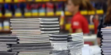 Pilhas de cadernos com capa flexível e espiral à venda em papelaria, com pessoas ao fundo desfocado