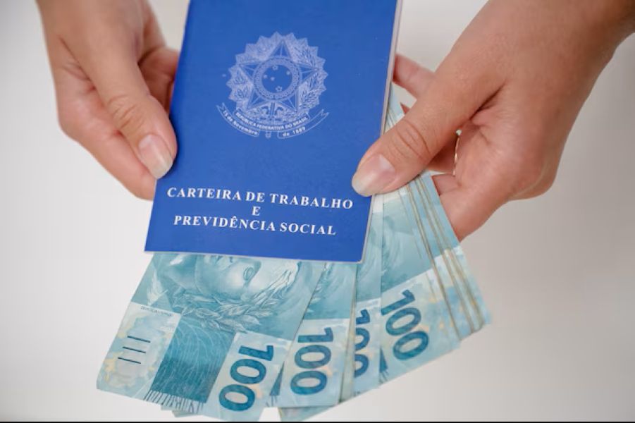 Carteira de Trabalho com notas de 100 reais, simbolizando os benefícios trabalhistas e o impacto do salário mínimo de 2026.