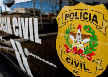 Emblema amarelo da Polícia Civil de Santa Catarina com elementos simbólicos como águia, trigo, café e estrela, afixado em carro policial preto com inscrição "Polícia Civil" ao fundo.