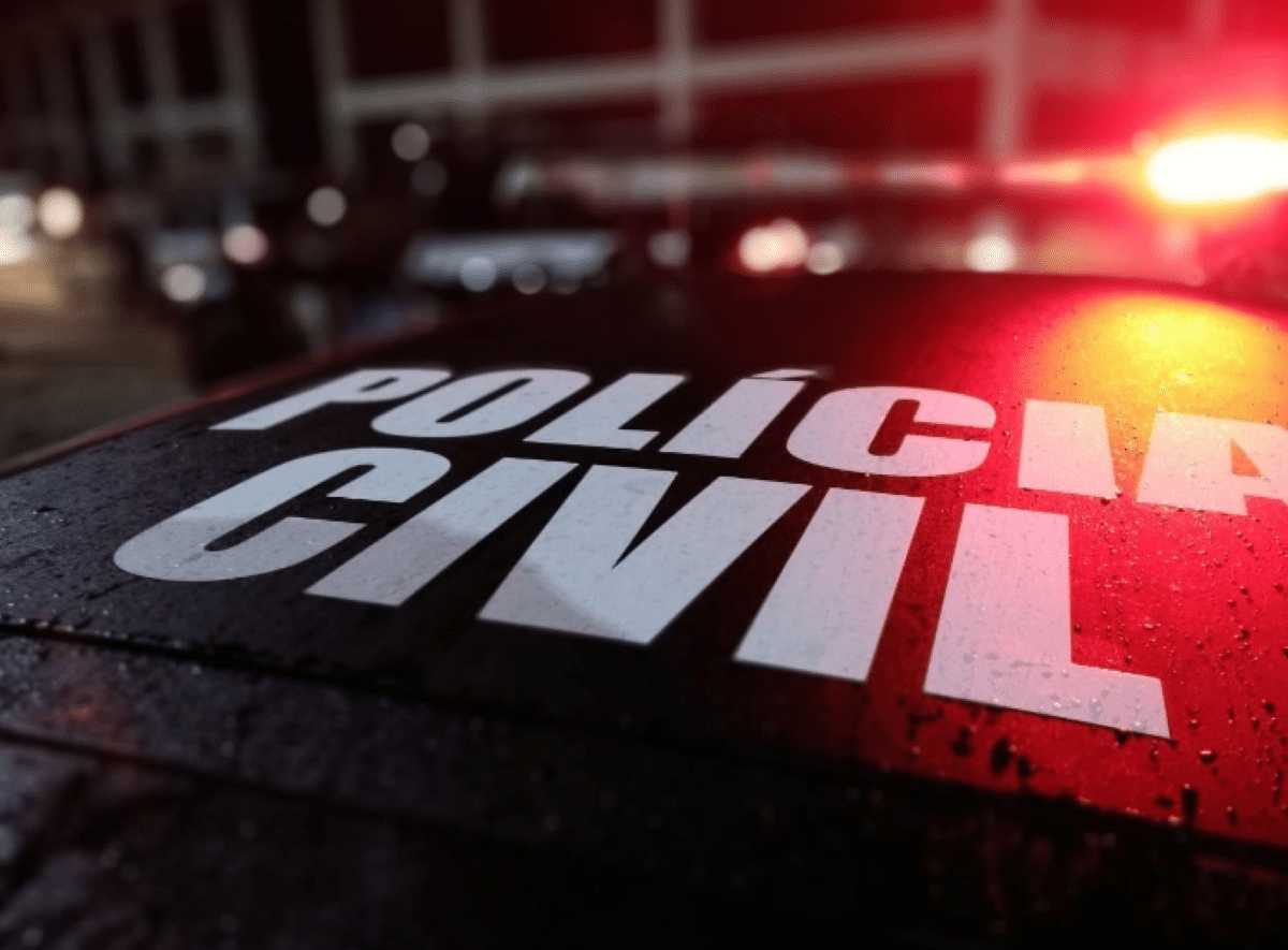 Inscrição "Polícia Civil" em letras brancas sobre teto de carro policial preto molhado, com reflexo de luz vermelha de sirene e fundo desfocado noturno.