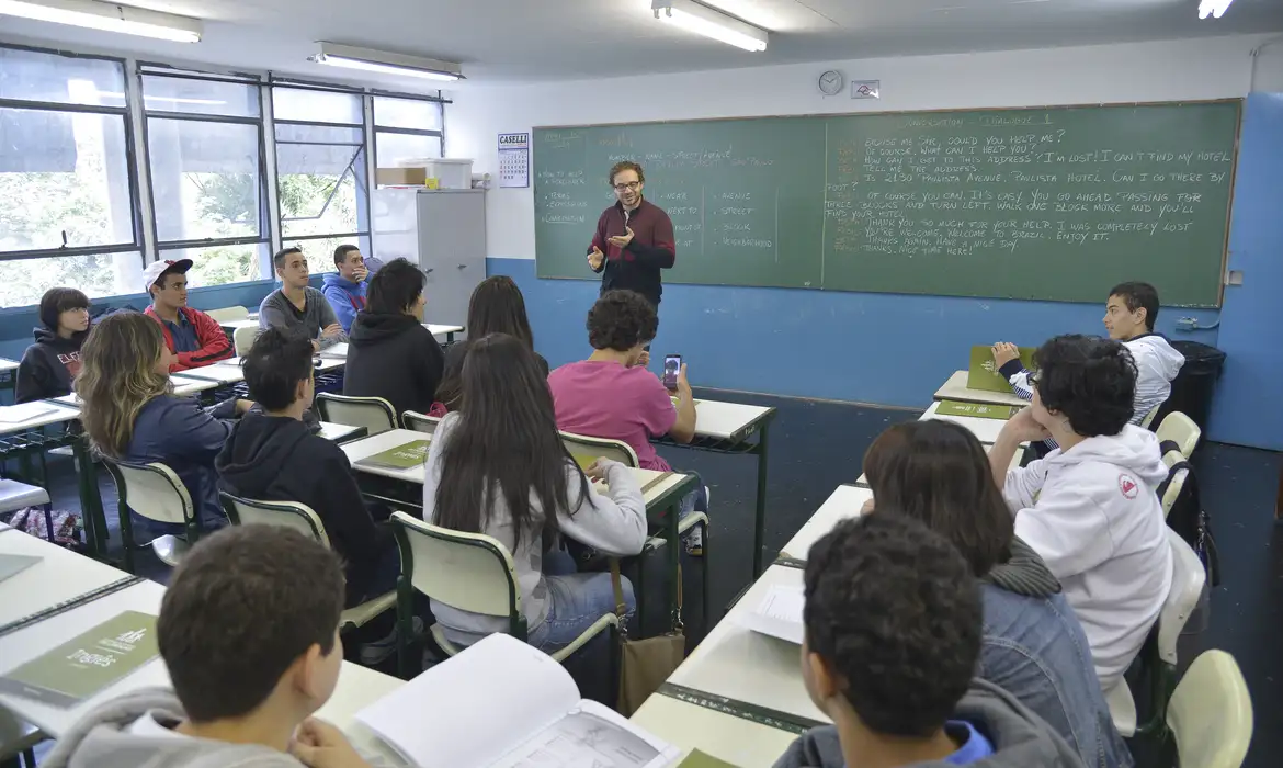 Aula de inglês com professor em sala de aula moderna Professor de inglês ensinando alunos sentados em carteiras numa sala de aula com quadro negro e luz natural
