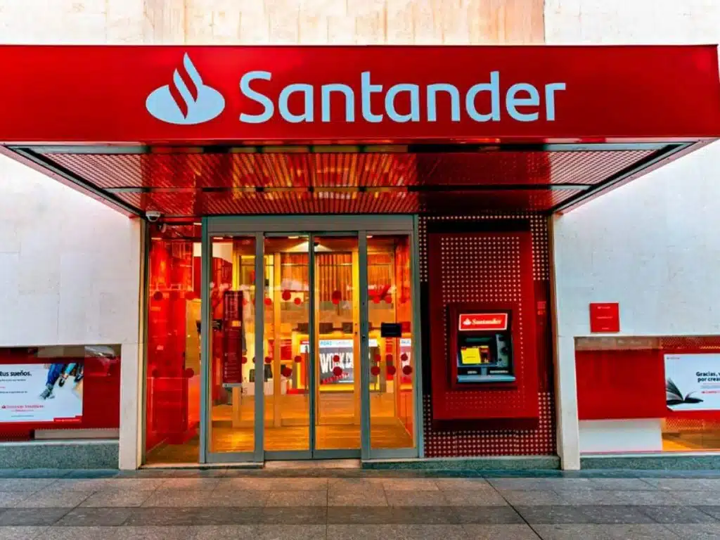 Agência Santander: pportunidades de carreira para 2026 Imagem da fachada de uma agência do Santander, destacando a entrada e o caixa eletrônico, simbolizando o ambiente bancário.