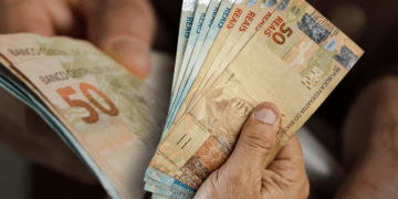 Pessoa segurando cédulas de R$ 50, representando o impacto positivo do reajuste do salário mínimo de 2026 na economia brasileira.